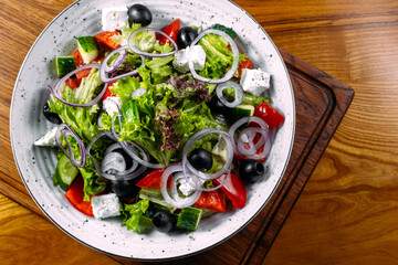 Fresh greek salad with tomato, cucumber, bel pepper , olives and feta cheese on black plate, top view, on the wood 