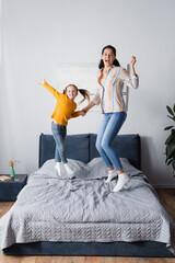 excited mother and daughter jumping on bed while looking at camera