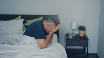 A middle-aged man suffers from a headache sitting on the bed.