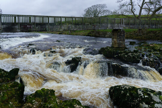 Rocky white water rapids with a wooden footbridge over it, Linton Falls, Grassington, North Yorkshire, UK. 