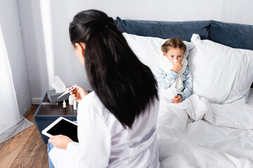 Obraz premium doctor looking at thermometer near diseased girl lying in bed
