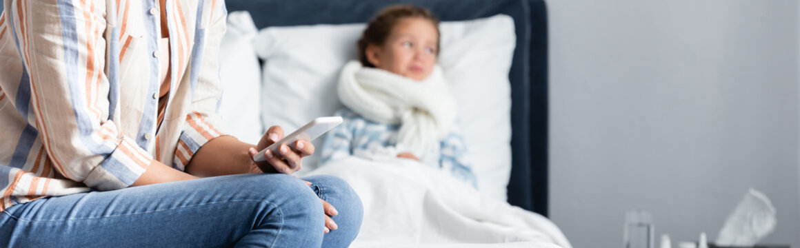 Woman Chatting On Mobile Phone Near Sick Child Lying In Bed On Blurred Background, Banner