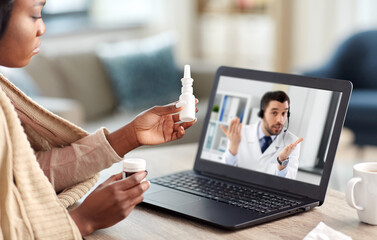 medicine, healthcare and technology concept - sick young african american woman having video call or online consultation with doctor on laptop computer at home and showing drugs