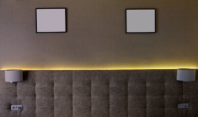 Illuminated backrest of a matrimonial bed with lamps on left and right side and two paintings above.