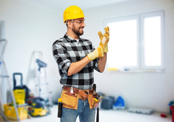 profession, construction and repair concept - happy smiling male worker or builder in helmet and gloves over room with building equipment background