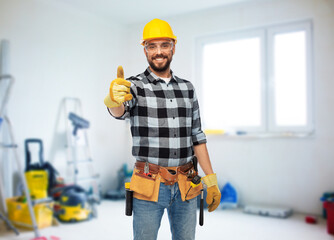 profession, construction and repair concept - happy smiling male worker or builder in helmet and goggles showing thumbs up over room with building equipment background