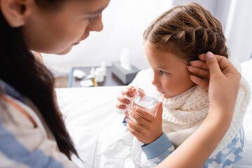 sick girl drinking water while mother touching her on blurred foreground