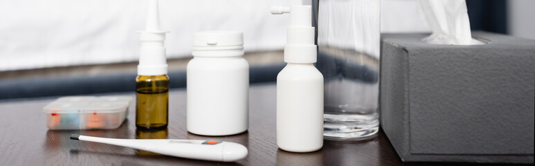 bedside table with nasal and throat sprays, thermometer, paper napkins and glass of water, banner