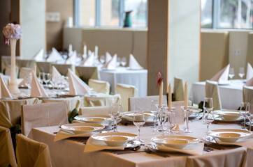 Indoor restaurant wedding tables beautiful decorated with candles , plates and cutlery prepared for the arriving guests