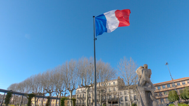French flag waving in the wind and the Monument to the Resistance and Deportation (liberation of Carcassonne from Nazi occupation), located on the square Gambetta, Carcassonne, France.