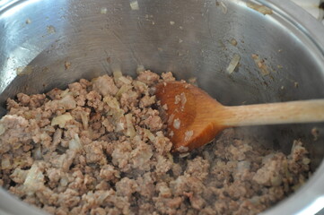 Cooking minced beef with a wooden spatula in a stainless steel frying pan. Stir fried onion and mince beef. frying pan with meat.