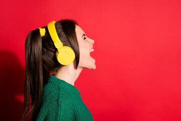 Photo of singing young woman dressed green knitted sweater headset looking empty space isolated red...