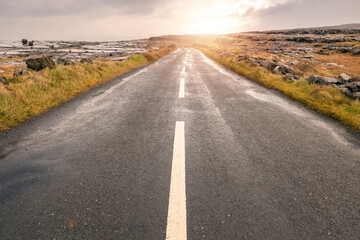 Fototapeta na wymiar Small narrow asphalt road to a mountain. Burren region, county Clare, Ireland. Low cloudy sky. Nobody,