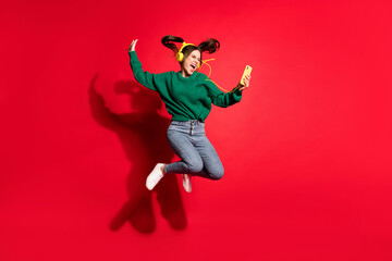 Full length photo of adorable young lady wear green knitted pullover listening music headphones dancing jumping isolated red color background