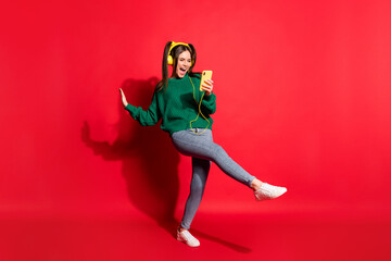 Full length photo of cute young lady wear green knitted pullover listening music headphones dancing singing isolated red color background
