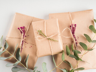 Zero waste holiday gifts wrapped in plastic free paper with dried floral decor on gray background.
