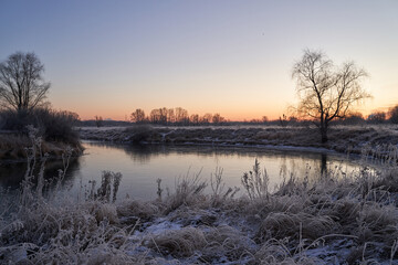 Fototapeta premium Breath of winter, first ice on the lake, dawn on a frosty morning with frost on the grass, close-up of frost, patterns on the first ice.