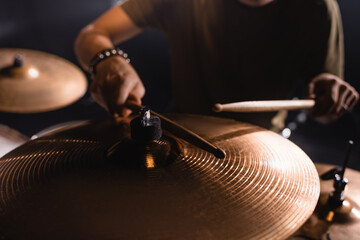 Cropped view of metal cymbals with blurred musician with drumsticks on background