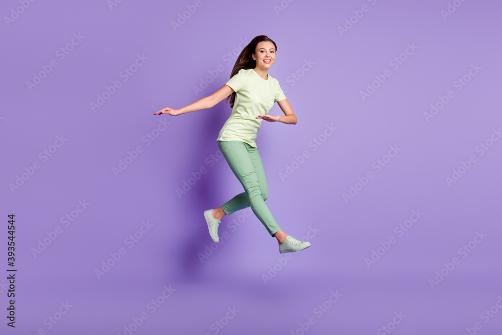 Poster Full length portrait of attractive lady jump have fun toothy smile wear green clothing isolated on purple color background