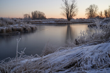 Breath of winter, first ice on the lake, dawn on a frosty morning with frost on the grass, close-up of frost, patterns on the first ice.