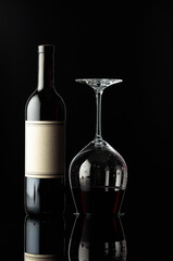 Bottle of red wine and an inverted glass with wine on a black background.