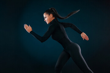 Strong athletic woman sprinter, running on black background wearing in the sportswear and headphones. Fitness and sport motivation. Runner concept.