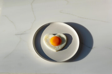 Fried eggs in the form of a heart on a white plate for breakfast. Marble background.
