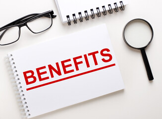 The word BENEFITS is written in a white notebook on a light background near the notebook,...