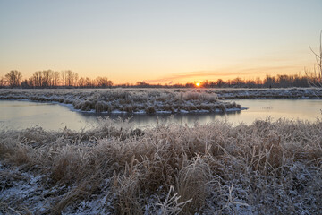Naklejka premium Breath of winter, first ice on the lake, dawn on a frosty morning with frost on the grass, close-up of frost, patterns on the first ice.