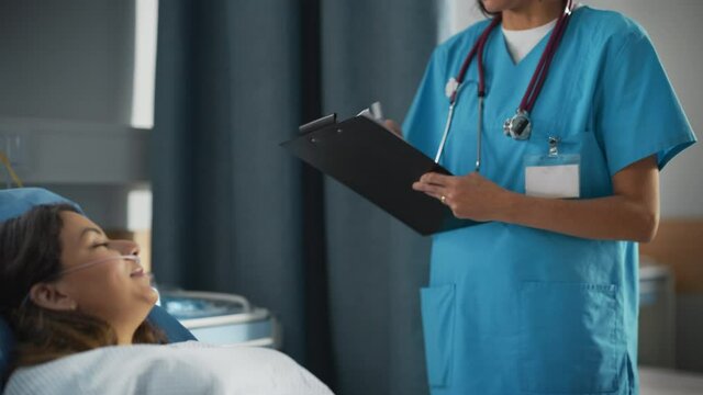 Hospital Ward: Friendly Hispanic Head Nurse Fills Medical History Form, Talks to Female Patient Recovering in Bed. Professional Nurse Helps Happy Woman Get Better after Surgery.Elevating Portrait Shot