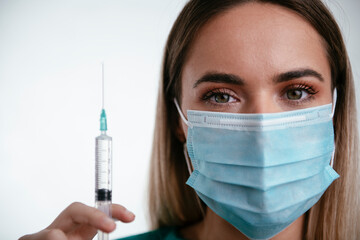 Beautiful female doctor with medical mask. Portrait of nurse with syringe in her hand.