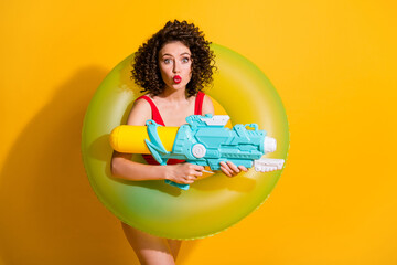 Photo of lovely pretty young excited girl hold water gun swim ring staring pouted lips play family weekend wear red singlet unclothed shoulders isolated vivid yellow color background