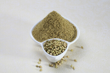 Coriander seeds and powder in a white ceramic bowl