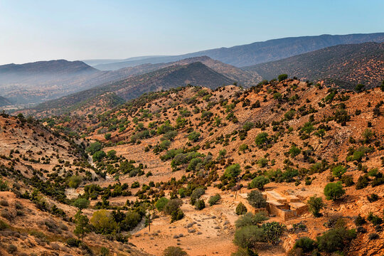 Landscape view of a Small River Crossing Atlas Mountains filled with Argania Spinosa Tree with Traditional Stone Built House Mountain.