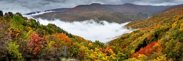 Panorama of foggy autumn landscape in the mountains with colored trees in Caldirola, Italy