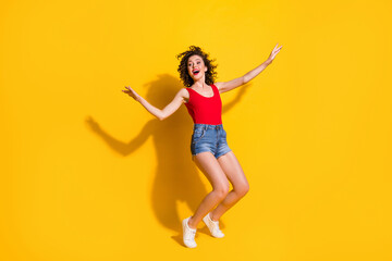 Full length body size photo of nice girl with curly hair dancing moving smiling satisfied at party singing standing tiptoes isolated on vivid yellow color background