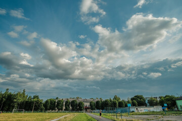 thick cloudy blue sky above the school yard and shady trees green