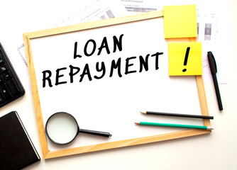LOAN REPAYMENT text is written on a white office board. Work table with office supplies.