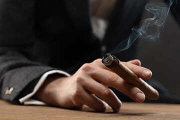 Close-up of man's hand resting on table  holding a lit cigar