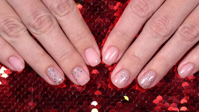 Closeup top view 4k video of female hands with professional pink manicure with glittering silver sparkles isolated on Christmas bokeh background. Modern festive minimal gel polish nail design.