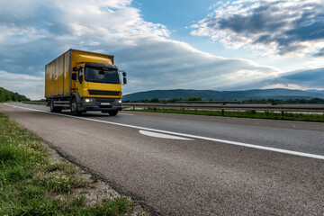 Highway transportation traffic scene with Yellow Cargo Delivery Truck speeding down the road
