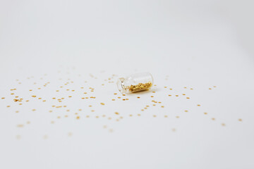 Spangles of gold and silver are scattered from bottles on a white background