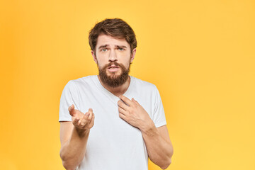 Bearded man in a white T-shirt gestures with his hands emotions studio yellow background