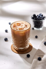 caffeine, objects and drinks concept - glass of ice coffee on cork drink coaster and blueberries