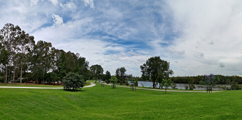 Obraz na płótnie Canvas Beautiful panoramic view of a park with green grass, tall trees and paved trail for walking and cycling, Reid Park, Parramatta Cycleway, Rydalmere, Sydney, New South Wales, Australia 