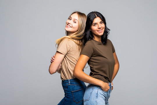 Two Young Women Standing Back To Back Againt The White Background.