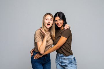 Portrait of two cheerful young women standing together isolated over gray background
