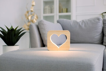 Wooden night lamp with heart picture, on gray monochrome sofa, at stylish light home living room interior. Home decor and lamps. Wooden hand made accessories