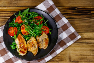 Fried chicken breast with salad of fresh arugula and cherry tomatoes on wooden table. Top view