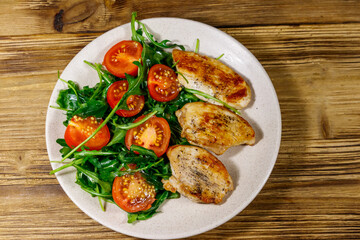 Fried chicken breast with salad of fresh arugula and cherry tomatoes on wooden table. Top view